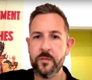 James McFadzean sits in a room wearing a dark shirt. The wall behind him is white and there is a poster with a person rising a bucking horse with words in French written on it