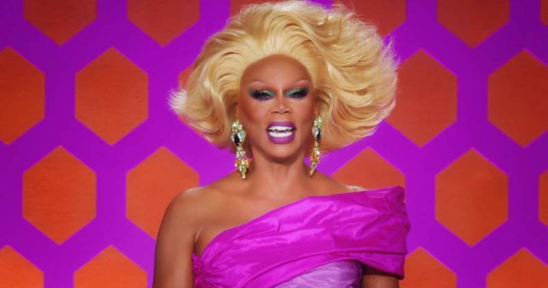 RuPaul laughs while wearing a pink off the shoulder dress, blonde wig and silver sparkly earrings while on the set of Drag Race All Stars 7