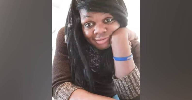 Brazil Johnson, a Black trans woman, wears a brown shirt and blue band on her write as she poses for a picture