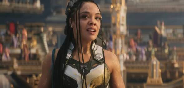 Tessa Thompson wears blue and white patterned armour as she stands in front of a crowded stadium as she plays the character Valkyrie in Thor: Love and Thunder