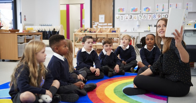 Teacher holding up a book in front of her class of elementary school kids sitting on the floor in a classroom