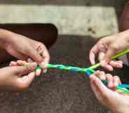 Two people hold fuzzy pipe cleaners which are coloured blue and green which they are braiding together