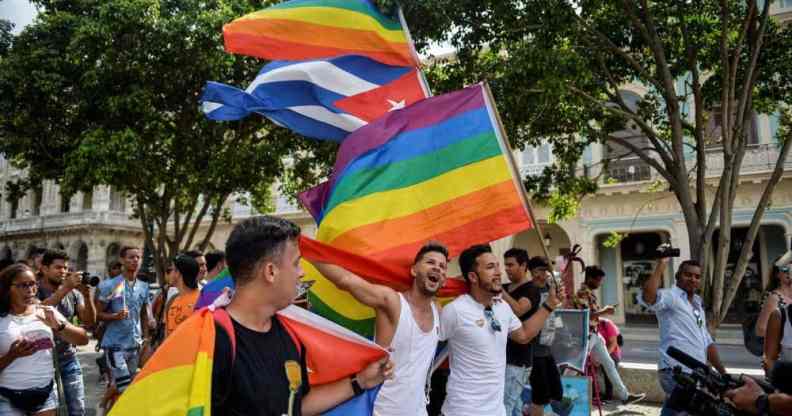 A crowd of people gather in the Prado avenue in Havana, Cuba holding up LGBTQ+ rainbow pride flags as well as the flag of Cuba