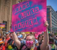 Participant seen holding a pink coloured sign with blue lettering that reads "trans lives matter" at a protest