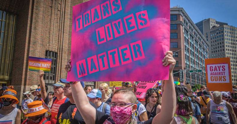 Participant seen holding a pink coloured sign with blue lettering that reads "trans lives matter" at a protest