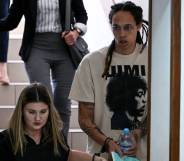 Brittney Griner wears a white t-shirt as she is handcuffed to another a person and led to a trial hearing in Russia