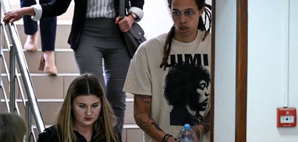 Brittney Griner wears a white t-shirt as she is handcuffed to another a person and led to a trial hearing in Russia