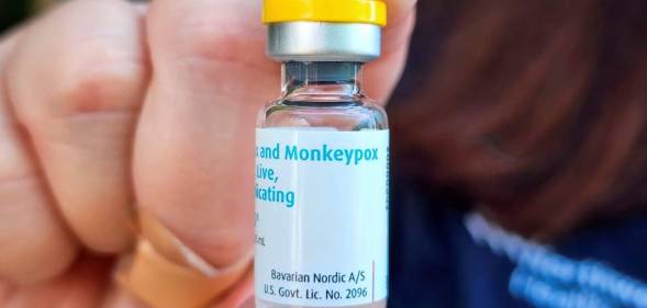 A person holds up a vile of a vaccine with the white label reading monkeypox