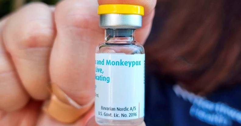 A person holds up a vile of a vaccine with the white label reading monkeypox