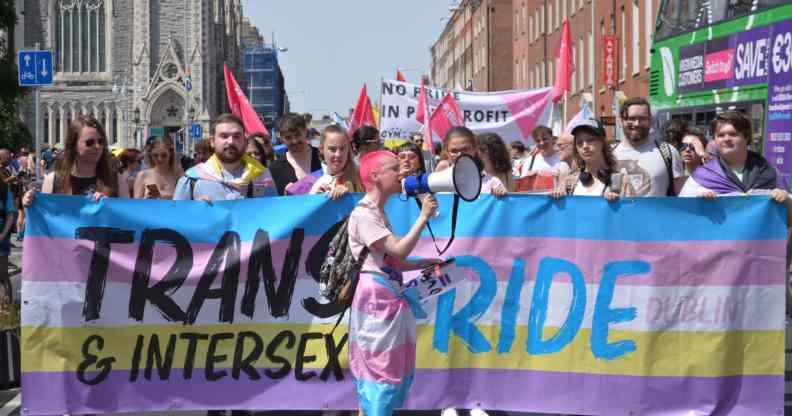 Crowds of at least a hundred (more not pictured), holding a banner that says Trans and Intersex Pride