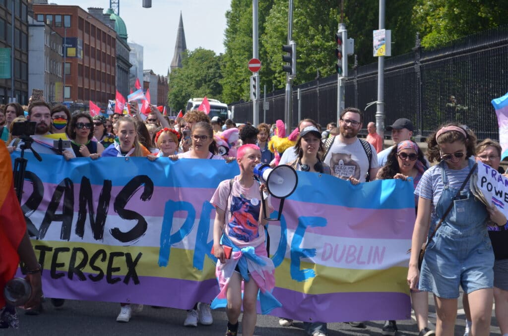 Ollie Bell holding a megaphone infront of the 'trans and intersex pride' banner