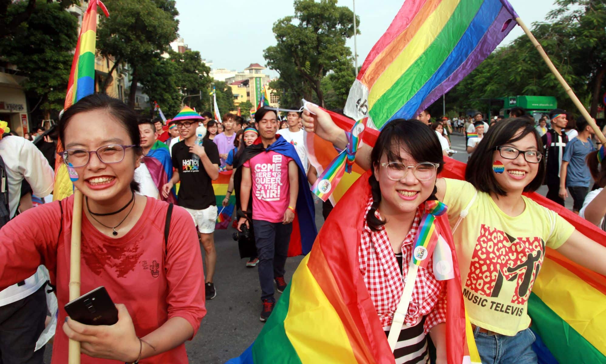 A crowd of people holding rainbow coloured items walk through a LGBTQ+ Pride parade in Vietnam