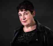 Joanne Harris wears a dark shirt and jacket while standing in front of a dark background