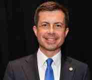 Pete Buttigieg smiles at the camera while wearing a suit and tie