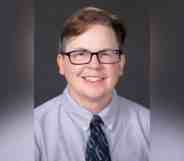 ESPN reporter MA Voepel wears a blue button up shirt with a dark tie as he stares at the camera