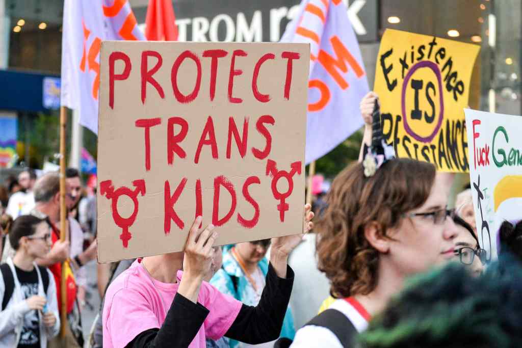 An activist raises a placard saying "protect trans kids" during a protest.