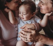 In this stock photo, two women hold a baby as it touches both of their faces