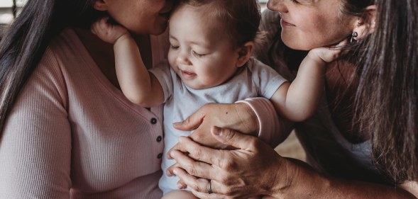 In this stock photo, two women hold a baby as it touches both of their faces