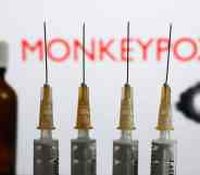 Medical syringes and a bottle are seen with 'Monkeypox' sign and monkeypox illustrative model displayed on a screen in the background in this illustration photo taken in Krakow, Poland.