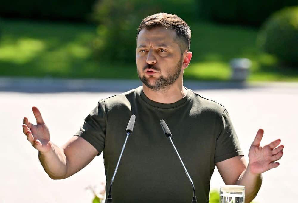 A photo shows Ukrainian President Volodymyr Zelensky wearing a dark green t-shirt as he speaks into two microphones