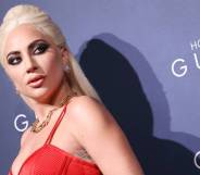 Lady Gaga wears a red dress as she stares over her shoulder at something positioned off camera