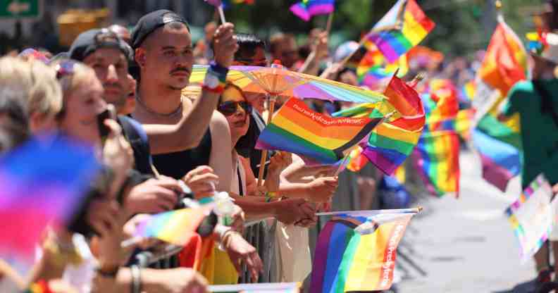 In this photograph, people wave rainbow Pride flags at a barrier