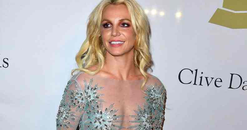 Britney Spears smiles at someone off camera while wearing a semi-transparent dress with blue crystal details on it