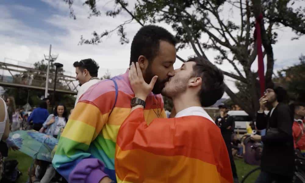 Two people wearing rainbow colours kiss in a park in Bogota, Columbia during a LGBTQ+ protest