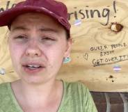 UpRising Bakery and Café owner Corrina Sac wears a light green shirt and red cap as she sits outside her business which has boards over the windows after the business was vandalised for planning to host a family-friendly drag event