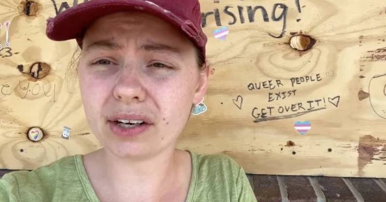 UpRising Bakery and Café owner Corrina Sac wears a light green shirt and red cap as she sits outside her business which has boards over the windows after the business was vandalised for planning to host a family-friendly drag event