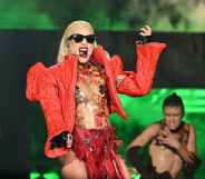 Lady Gaga performing on stage, wearing a thick red jacket with pointy shoulders over a see-through body