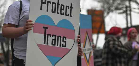 An activist holds a placard with words 'Protect Trans Youth'.