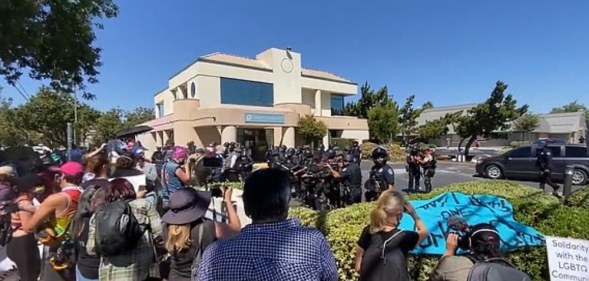 In this video screenshot, police circle protesters outside a building