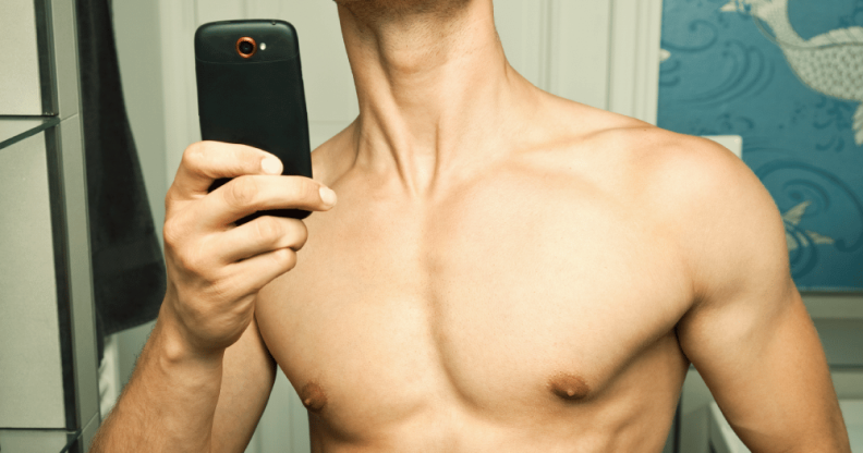 A topless man taking a mirror selfie, his face cropped out