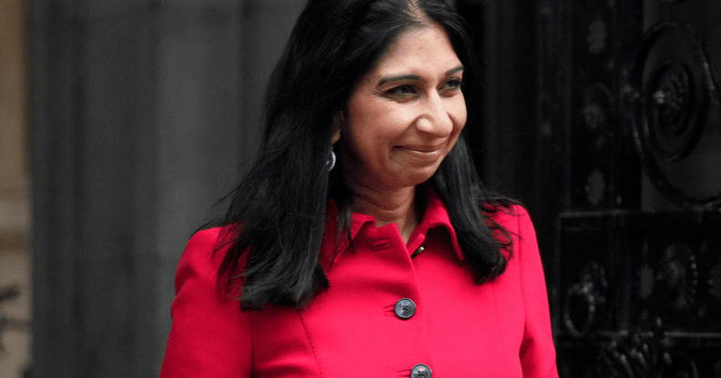 Suella Braverman wears a pink-red outfit as she smiles at someone off camera