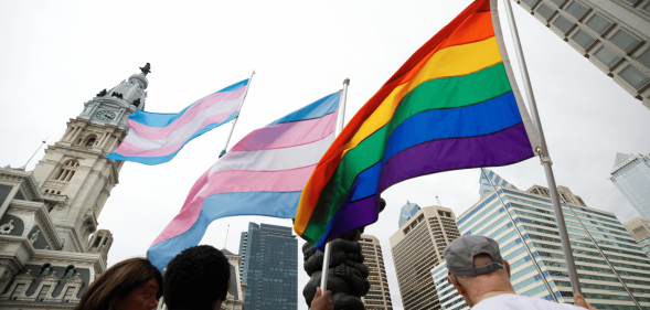 Several people hold up LGBTQ+ Pride and trans Pride flags