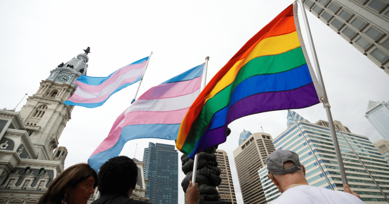 Several people hold up LGBTQ+ Pride and trans Pride flags