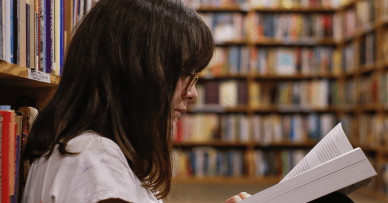 A young person reads a book in a school library like setting