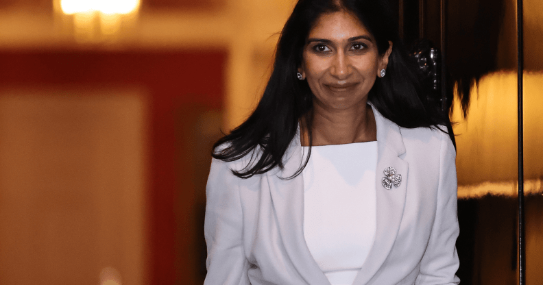 Suella Braverman wears a white and grey outfit as she walks out a doorway