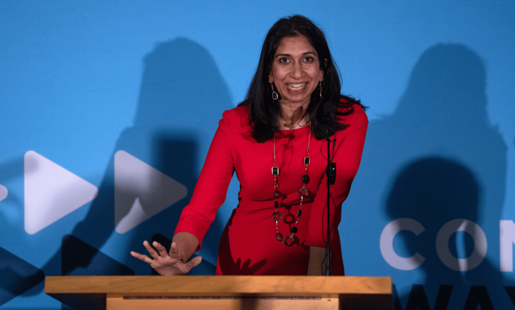 Suella Braverman wears red as she stands a podium