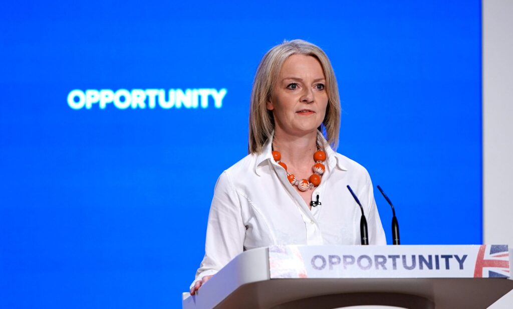 Liz Truss stands at a podium with the word 'opportunity' written on it