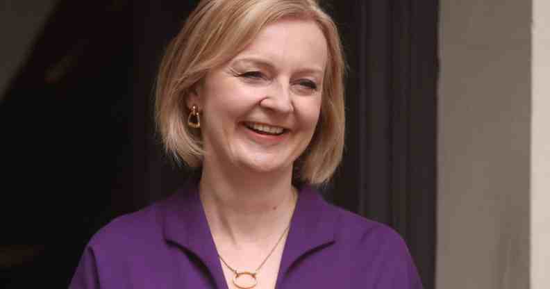 Liz Truss smiles as she stands outside a building wearing a purple outfit