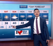 A still of NY1 weatherman Erick Adame wearing a navy suit, white shirt and red tie giving one of his TV weather broadcasts