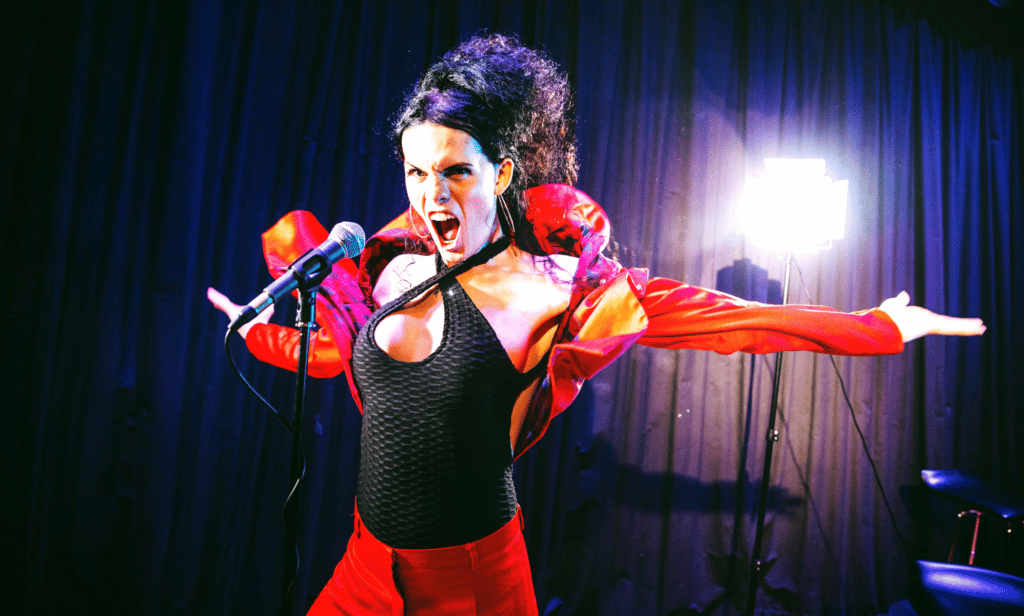 Jordan Gray wears a black and red outfit as she sings into a microphone while on stage