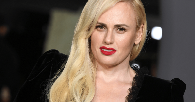 Rebel Wilson wears a black dress with her blonde hair styled over one shoulder