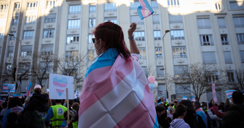 A person wears a trans Pride flag and waves a matching flag in their hand during a protest