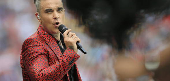 Robbie Williams wears a red animal-print patterned outfit as he sings into a microphone