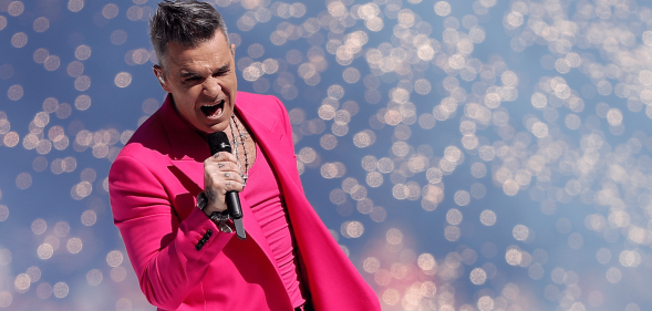 Robbie Williams wears a pink outfit as he sings into a microphone