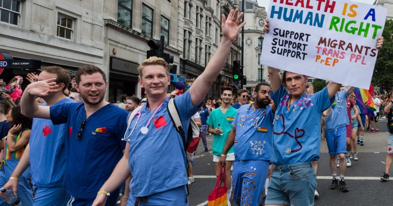 A group of NHS England doctors march during a Pride parade. One is wearing a sign that reads: "HEALTH IS A HUMAN RIGHT. Support Migrants, Support Trans PPL, Support PrEP"