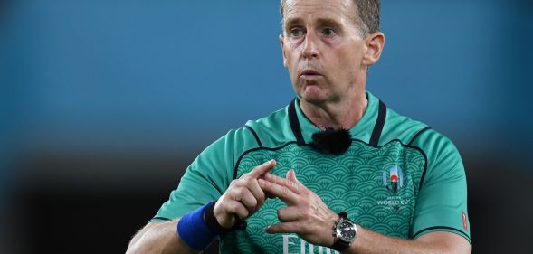 Nigel Owens makes a gesture while refereeing a rugby match in a green shirt.